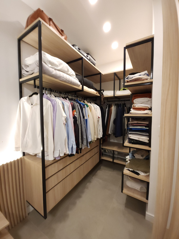Closet com estrutura aparente de aço preto, prateleiras e cabideiros em madeira clara, camisas e gavetas organizadas.