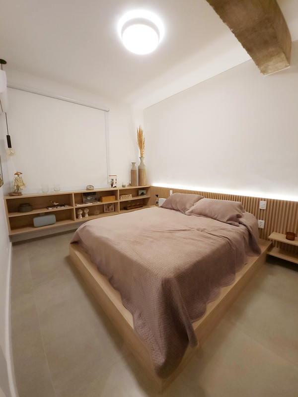 Quarto com cama king, cabeceira ripada em madeira clara, prateleiras baixas com objetos e iluminação indireta na sanca.